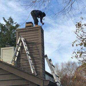 A worker on a ladder on a roof performing chimney service for Granite State Chimney in Manchester, NH