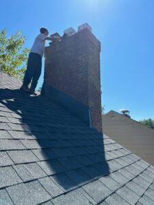 A worker on a roof performing repairs or maintenance on a brick chimney under a clear sky by Century Chimney Sweep and Repair in Cleveland, OH