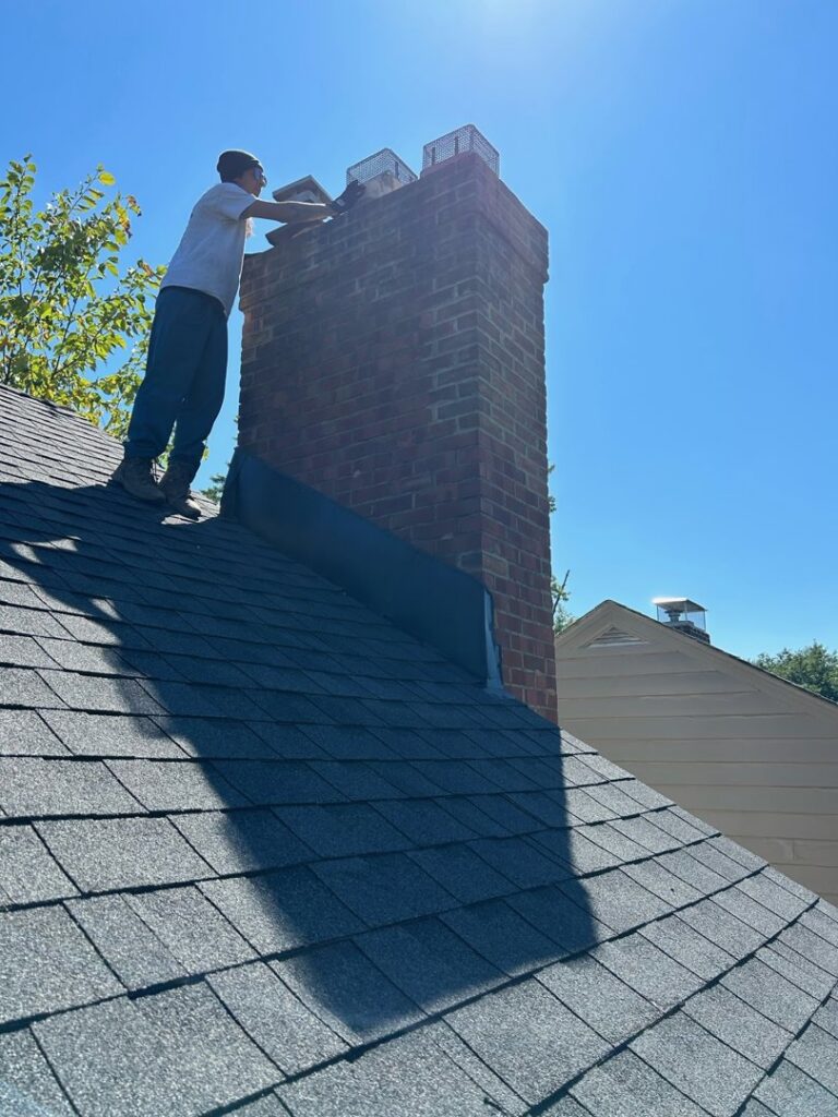 A worker on a roof performing repairs or maintenance on a brick chimney under a clear sky by Century Chimney Sweep and Repair in Cleveland, OH