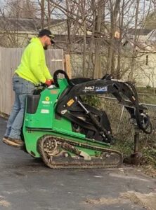 A worker operating a mini skid steer with an auger attachment for fence post installation by Stapleton Fencing LLC in Lexington, KY.