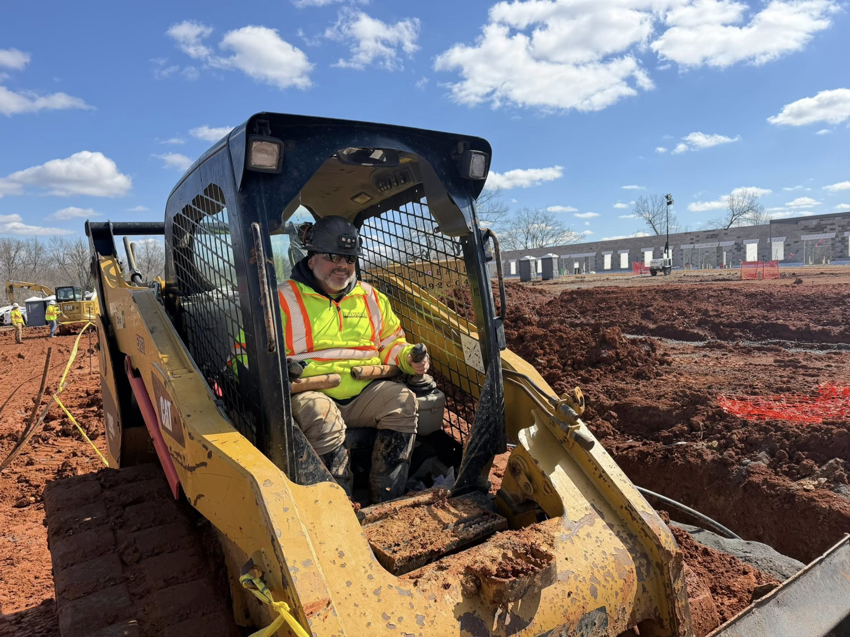 A worker operating a skid steer loader for geothermal ground loop installation at Jackson Geothermal in Mansfield, OH.