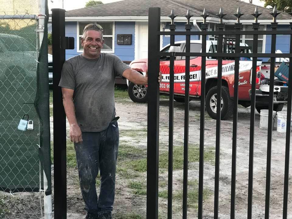 A Fencing & Railing 2 Corp worker proudly stands next to a newly installed black ornamental iron gate in Orlando, FL.