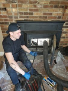 A worker performing an interior chimney sweep with tools and a vacuum hose by Clean Sweep Chimney Service in Saint Charles, MO.