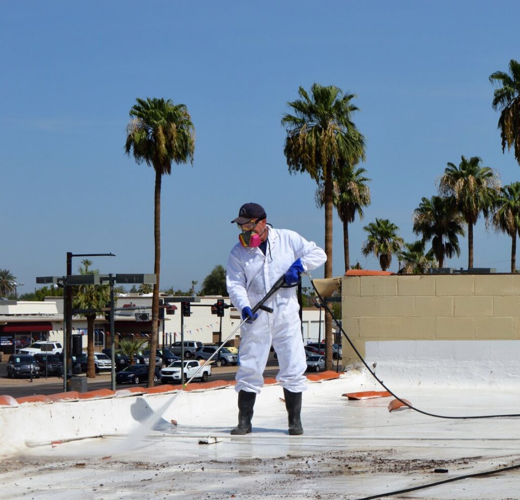 A worker in protective gear power washing bird droppings from a rooftop, a service offered by Pigeon Control Phoenix AZ in Glendale, AZ.
