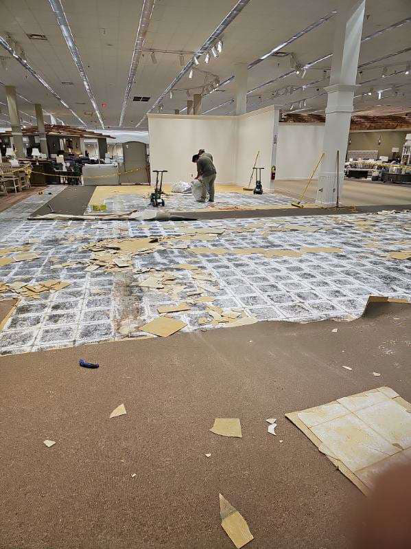 A worker removing old carpet and cleaning debris in a commercial space by Universal Flooring LLC in Las Cruces, NM
