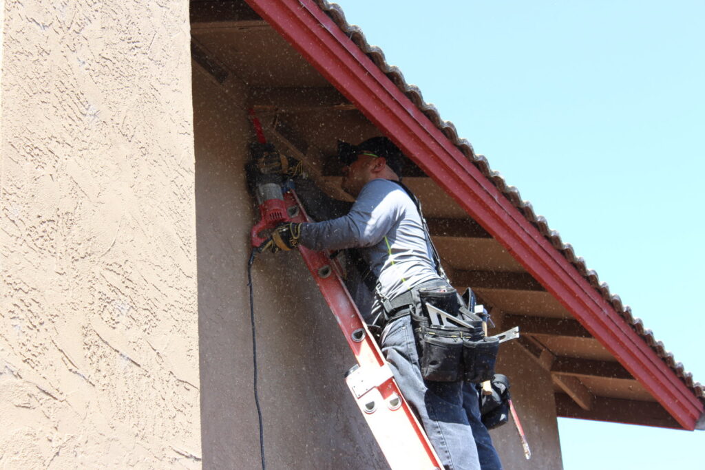 A worker on a ladder using a power tool to repair termite damage on a house in San Marcos, CA, by United Termite Control.