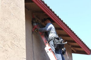 A worker on a ladder using a power tool to repair termite damage on a house in San Marcos, CA, by United Termite Control.