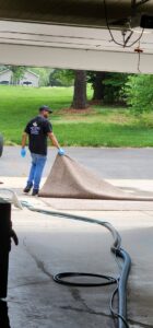 A worker rolling up a carpet with cleaning hoses visible, performed by Drew's Cleaning and Restoration in Jamestown, NC.