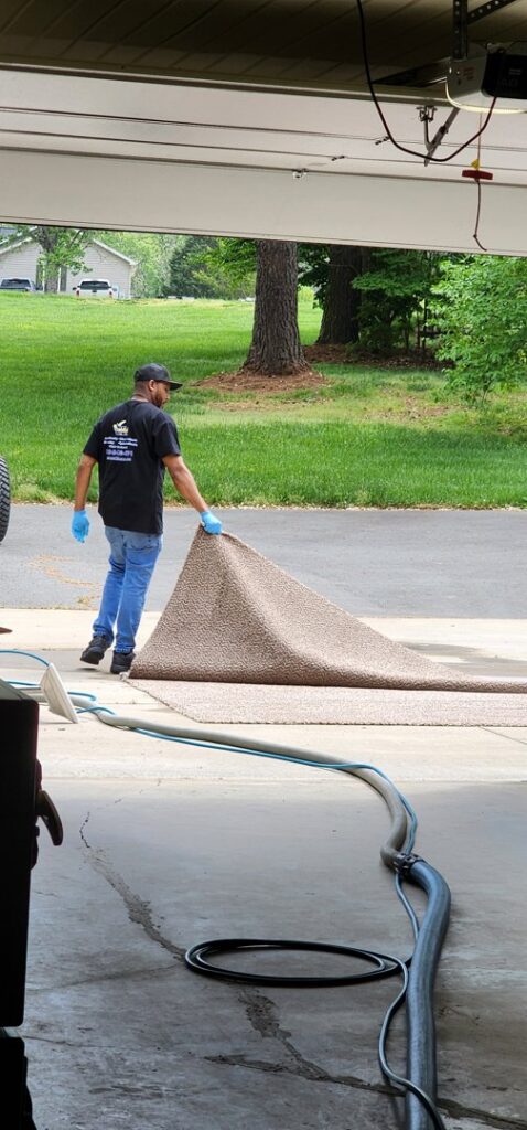 A worker rolling up a carpet with cleaning hoses visible, performed by Drew's Cleaning and Restoration in Jamestown, NC.