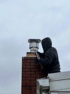 A worker on a roof applying sealant around a new chimney cap, performed by Maximum Energy Savers in Philadelphia, PA