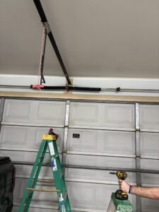 A worker on a ladder servicing the top section of a residential garage door, demonstrating expertise from Cajun Doors & More in Lafayette, LA.