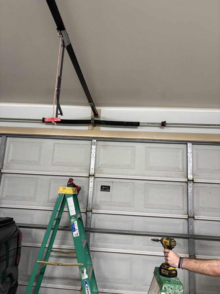 A worker on a ladder servicing the top section of a residential garage door, demonstrating expertise from Cajun Doors & More in Lafayette, LA.