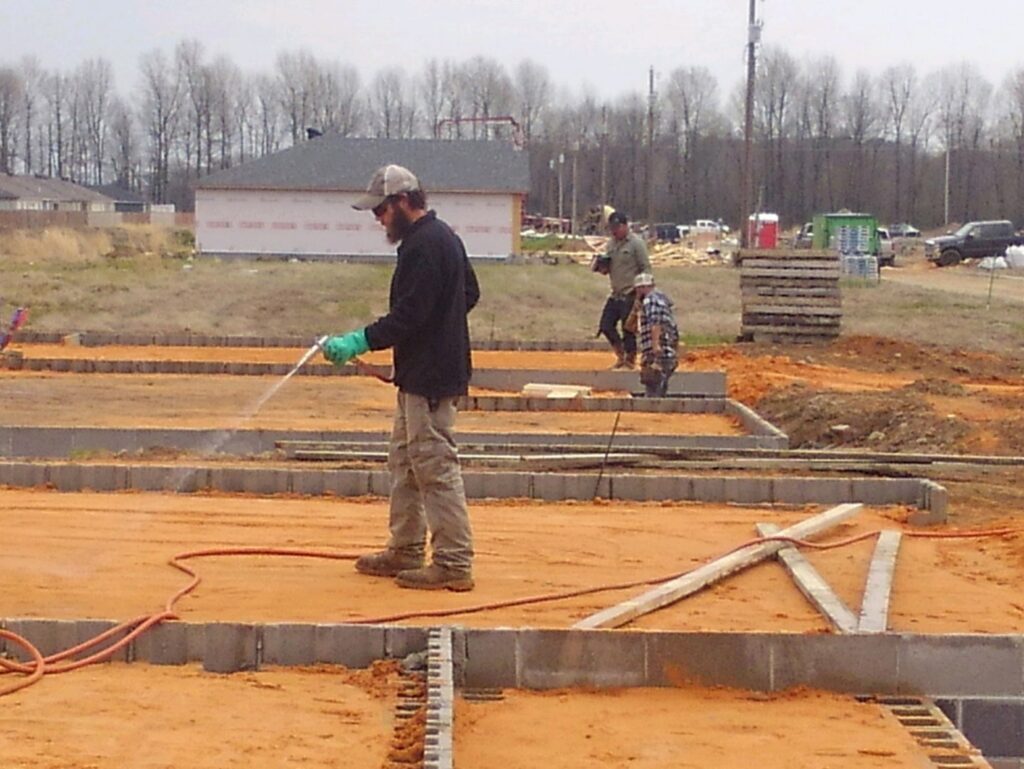 A worker spraying a liquid treatment on a building foundation for pest control at Clifft Lawn & Pest Management in Jonesboro, AR.