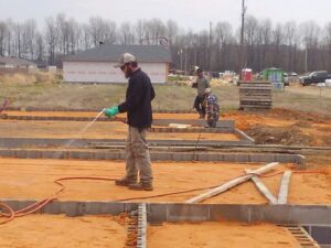 A worker spraying a liquid treatment on a building foundation for pest control at Clifft Lawn & Pest Management in Jonesboro, AR.