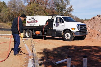 A Reliable Termite of OKC technician spraying the ground next to a large pest control truck in Oklahoma City, OK.