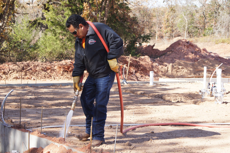 A worker from Reliable Termite of OKC applying treatment around a new construction foundation in Oklahoma City, OK.