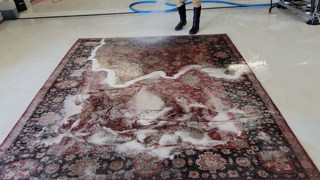 A worker spraying cleaning solution onto a large patterned rug at Advanced Cleaning Systems in Atlanta, GA.