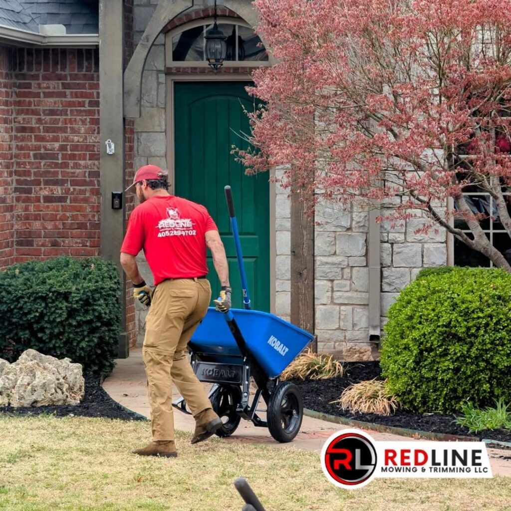 A Redline Mowing & Trimming worker spreading mulch in a garden bed as part of a landscaping service in Stillwater, OK.