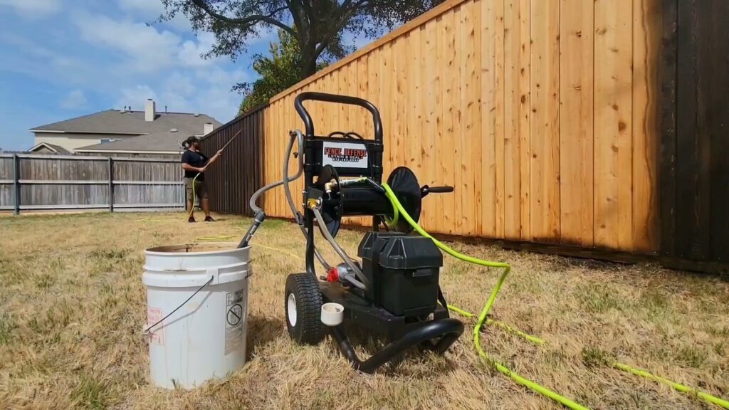 A worker staining a wooden fence with a sprayer, showing before and after sections, by Fence Defense in Plano, TX