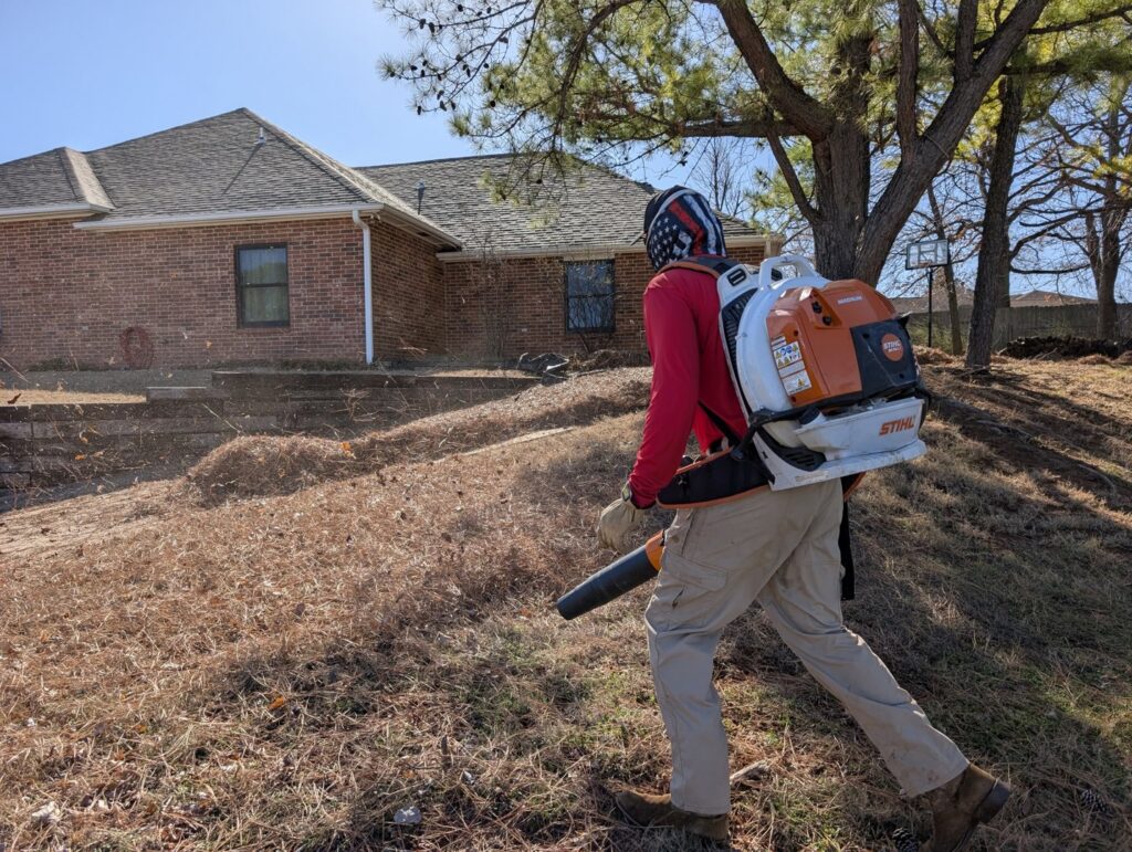 A Redline Mowing & Trimming worker using a Stihl backpack leaf blower for a thorough leaf cleanup in Stillwater, OK.