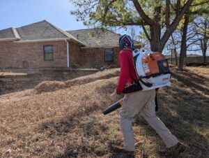 A Redline Mowing & Trimming worker using a Stihl backpack leaf blower for a thorough leaf cleanup in Stillwater, OK.