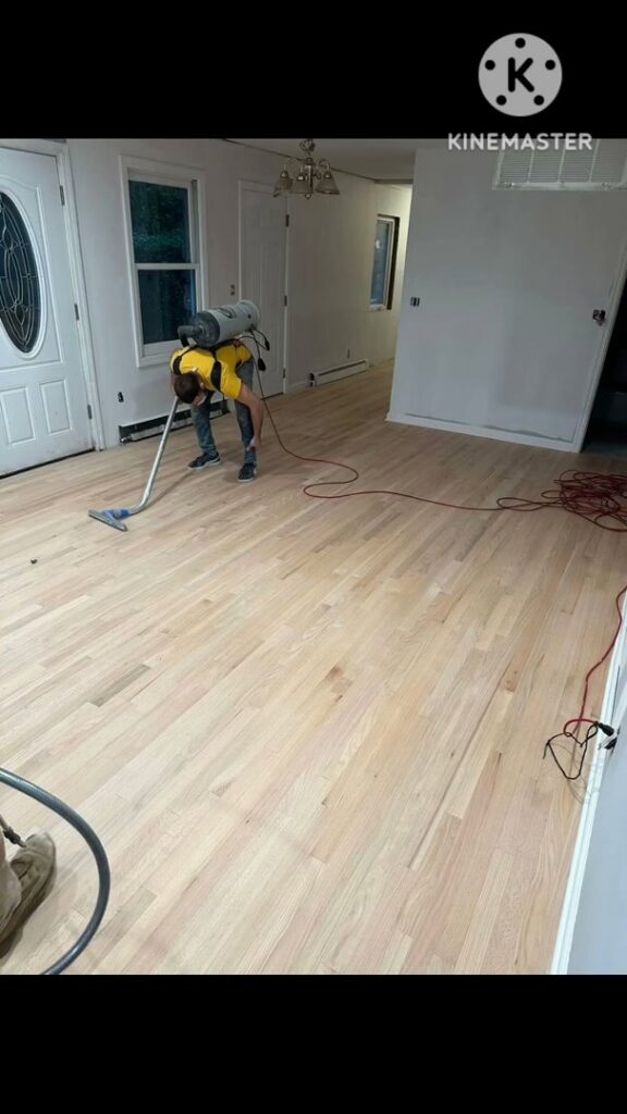 A worker vacuuming a newly installed hardwood floor as part of the finishing process by Isad Home Floor in Bridgeport, CT.