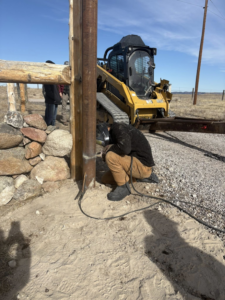 A worker welding a metal fence post to a wooden post during a fencing job by Cool Hand Fencing and Wyo War Wagons in Laramie, WY.
