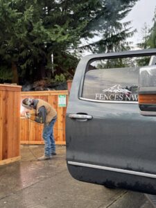 A Fences NW LLC worker welding a metal fence component next to a wooden fence in Spanaway, WA