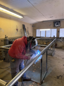 A worker welding a metal fence frame or gate in a workshop for Wayside Fences in Brattleboro, VT.