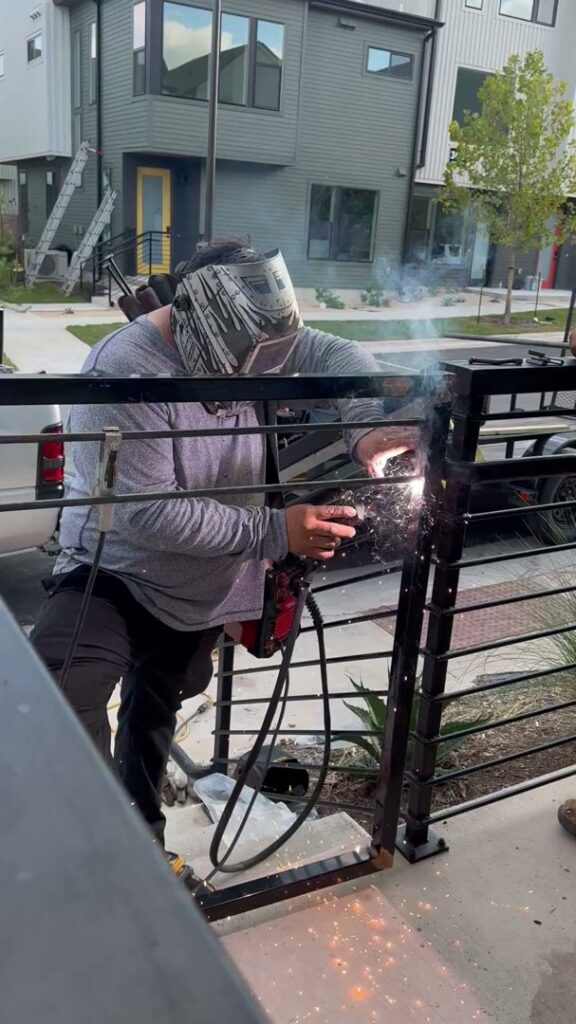A skilled worker welding a metal fence or railing, demonstrating precision work by Stand Strong Fencing of East Austin, TX.