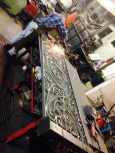 A worker welding an ornate wrought iron fence panel at Ideal Wrought Iron in Detroit, MI