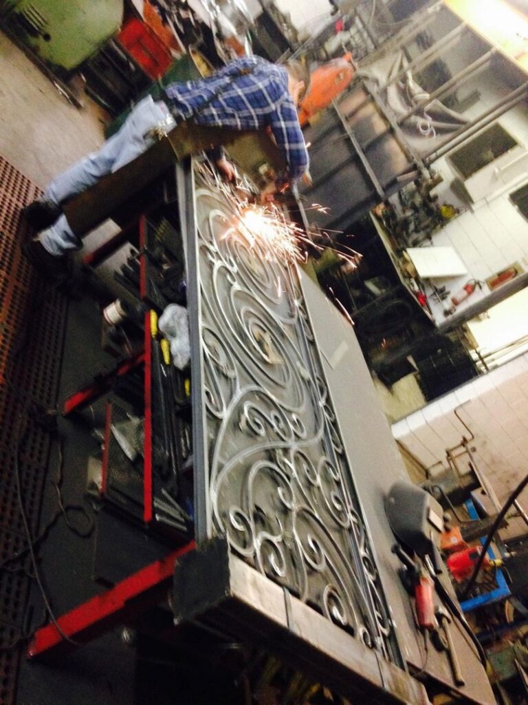 A worker welding an ornate wrought iron fence panel at Ideal Wrought Iron in Detroit, MI