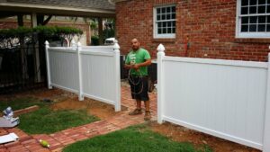 A worker standing next to newly installed white vinyl fence panels by G L Fence & Remodeling in Arlington, TX.