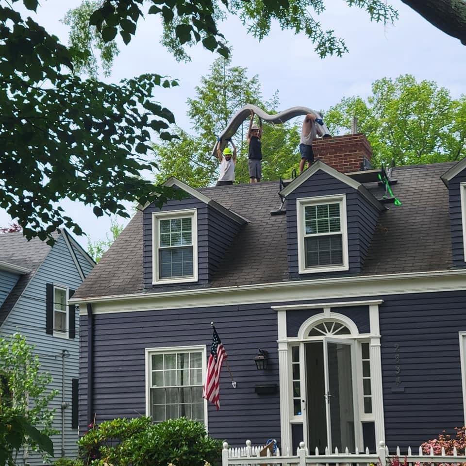 Workers on a roof carrying a large flexible chimney liner towards a chimney for installation by Century Chimney Sweep and Repair in Cleveland, OH
