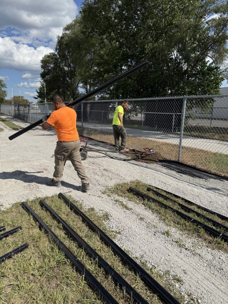 Workers carrying fence posts for a chain-link fence installation by Premier Fence LLC in Canton, MA.