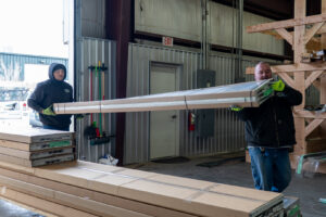 Two Prutch's Garage Door workers carrying a long, packaged garage door panel or track inside a warehouse in Colorado Springs, CO
