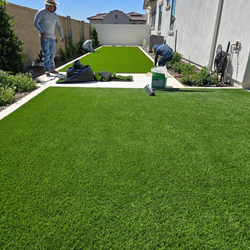 Workers installing artificial turf in a backyard, a service provided by AZ Hardscape & Landscape LLC in Phoenix, AZ.