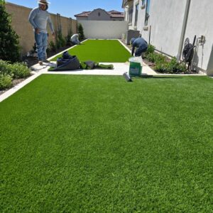 Workers installing artificial turf in a backyard, a service provided by AZ Hardscape & Landscape LLC in Phoenix, AZ.
