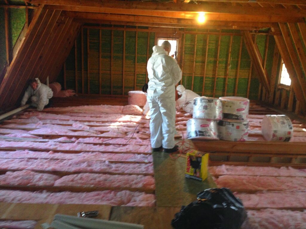 Workers in protective suits installing new insulation in an attic, a service provided by Wildlife Extractors in Bridgewater, MA.