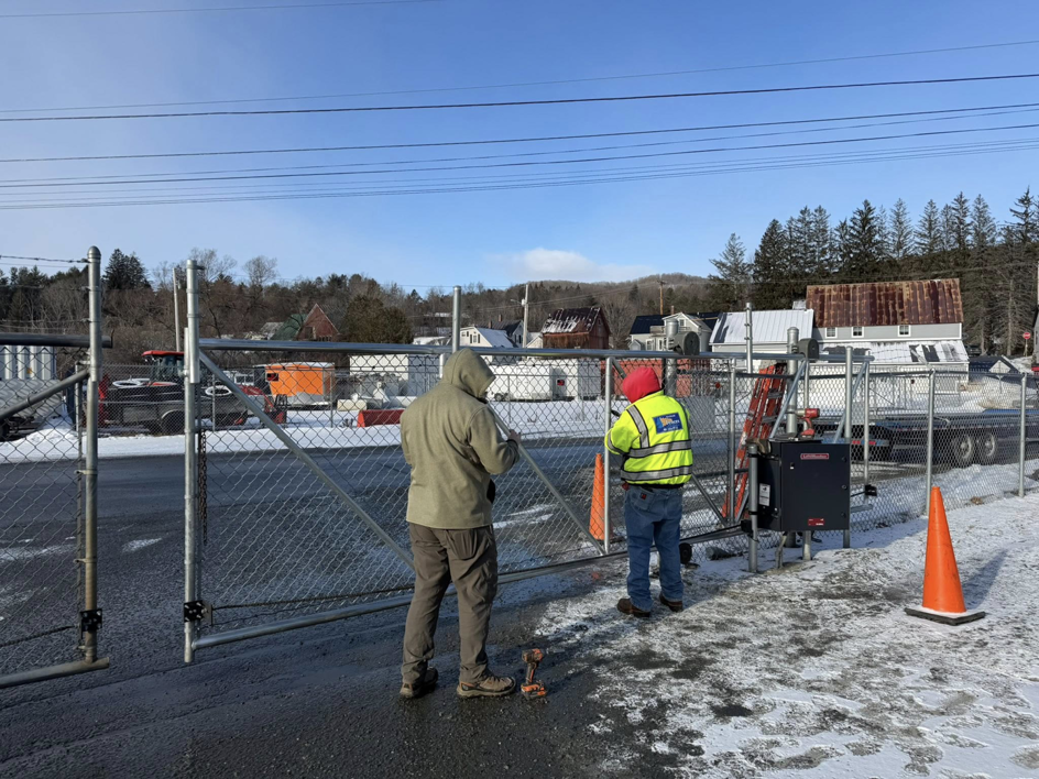 Two workers installing an automatic chain-link fence gate for a client of Wayside Fences in Brattleboro, VT.