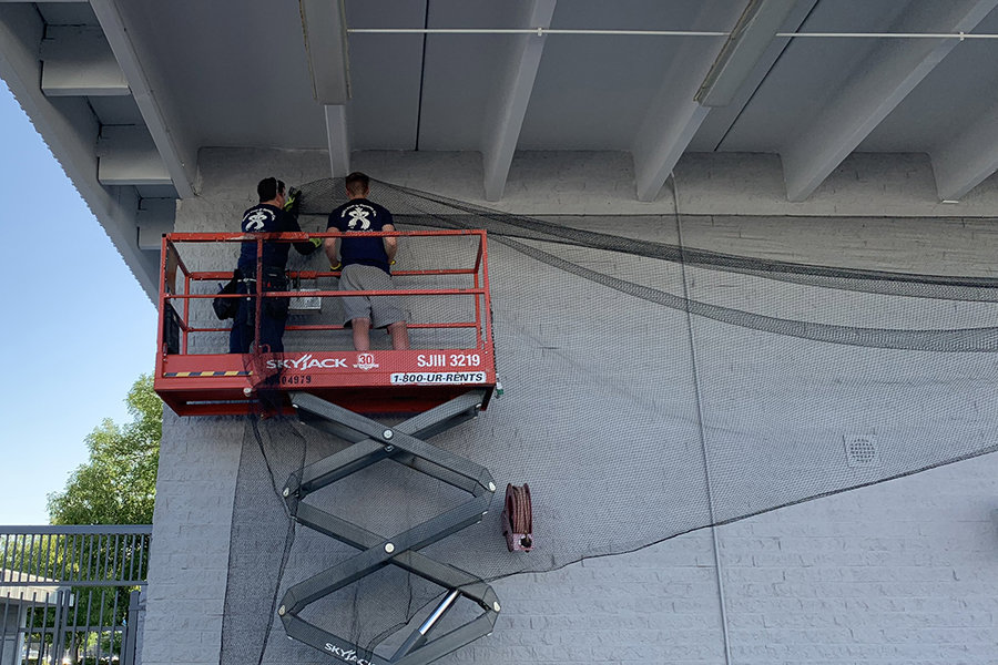 Two workers on a scissor lift installing bird netting on a building for effective pigeon control by Pigeon Control Phoenix AZ in Glendale, AZ.
