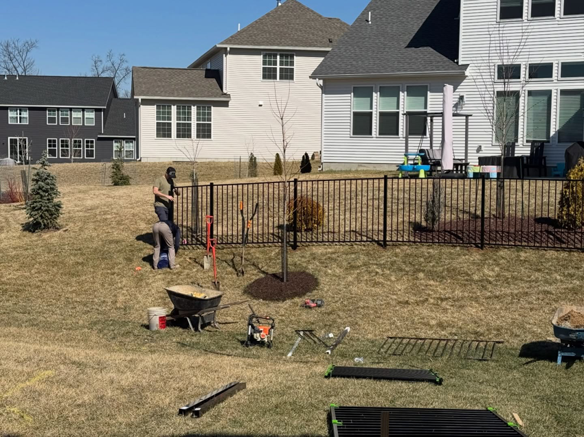 Workers installing a black aluminum fence in a residential backyard for a client of BK FenceWorks in Wentzville, MO.