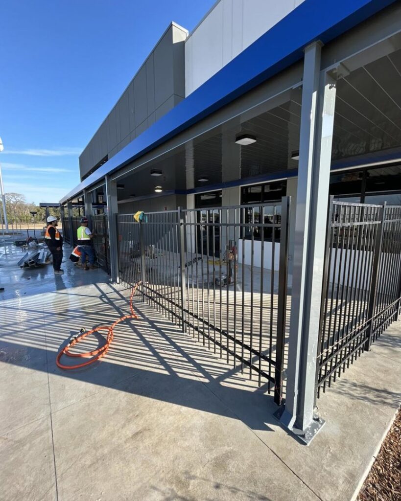Workers installing a black ornamental metal fence outside a commercial building by Georgia Select Fence in Senoia, GA.