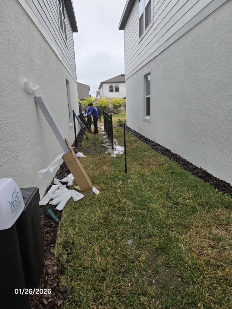 Workers installing a black metal fence between two residential homes for Elite Fence and Outdoor of Tampa Bay in Tampa, FL.