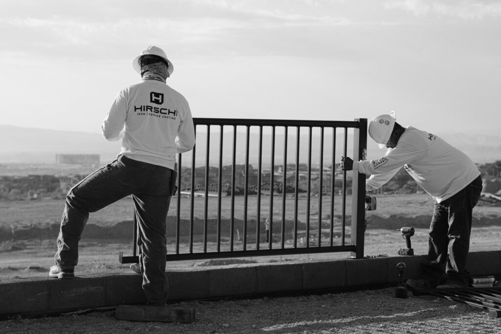 Two workers from Hirschi Iron installing a black metal fence or railing on a retaining wall in North Las Vegas, NV.