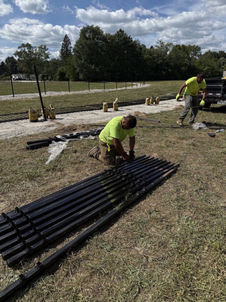 Workers installing a black metal fence, preparing posts on site for Premier Fence LLC in Canton, MA.