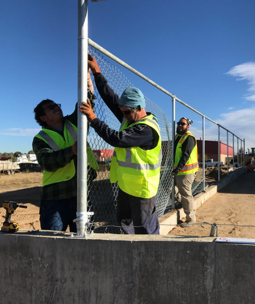Three workers installing a chain-link fence on a commercial property, by Colorado Springs Fence Company in Colorado Springs, CO.