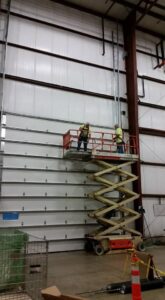 Two workers on a scissor lift installing a large commercial overhead door for Tri County Overhead Door Service Inc in New London, WI