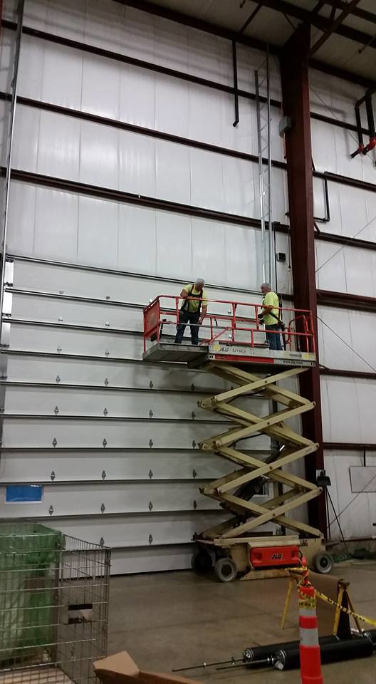 Two workers on a scissor lift installing a large commercial overhead door for Tri County Overhead Door Service Inc in New London, WI