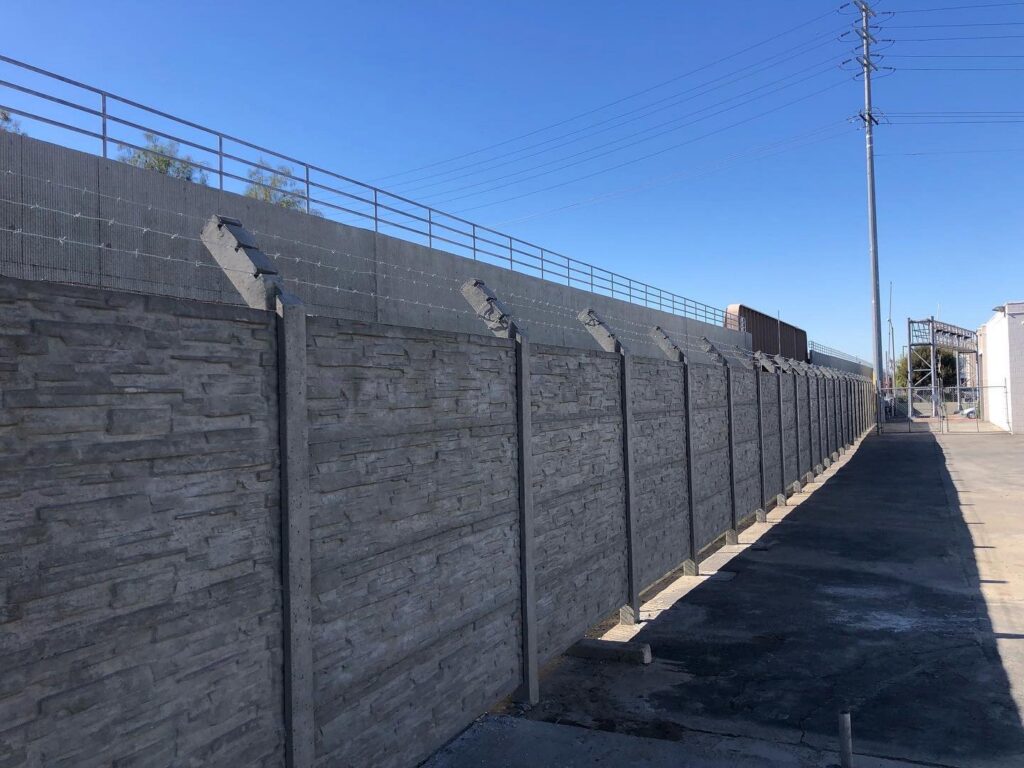 Workers installing concrete fence panels on a sloped residential property for StackWall Manufacturing in Pomona, CA.